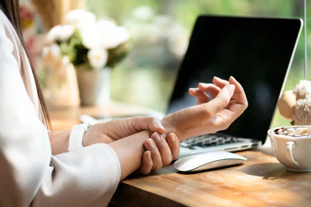 Mulher segurando a dor no pulso por usar o computador. Dor nas mãos como síndrome de escritório por doença ocupacional.